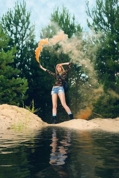 Lost hiker wagging smoke flare to signal for help on outer wood standing by the lake