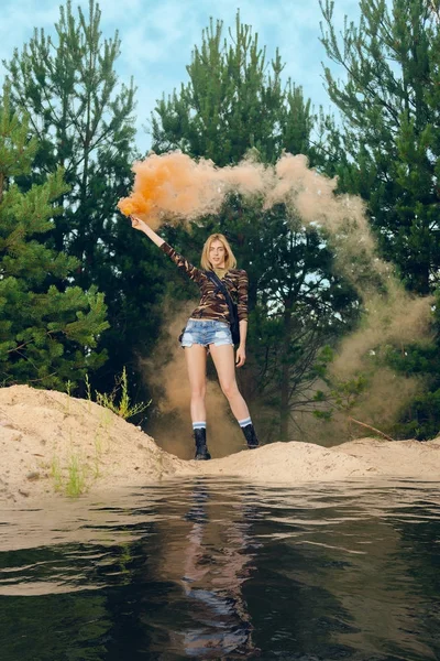 Lost hiker wagging smoke flare to signal for help on outer wood standing by the lake