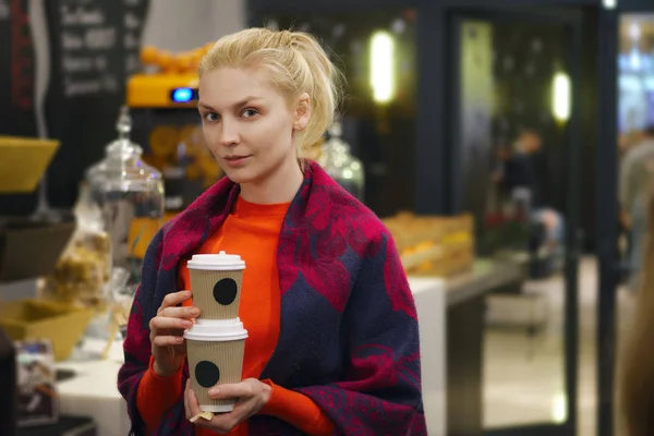 Pretty student in cafeteria near counter holding two cups of coffee