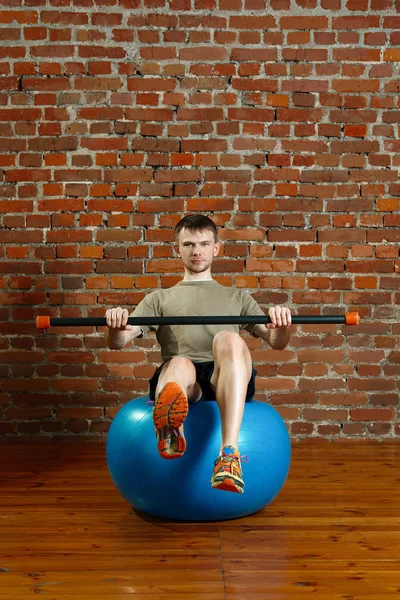 Athletic man doing balancing exercises over the gym ball with gy