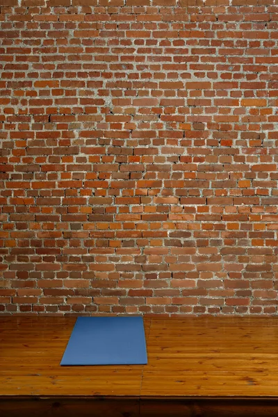 Gym mat on wooden podium with brick wall on background — Stock Photo, Image