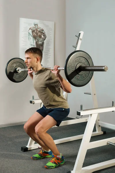 Atletisk man gör knäböj övning med hantel. Stark man gör skivstång knäböj. — Stockfoto