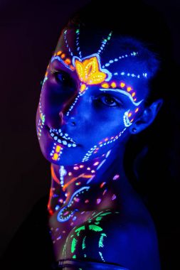 Yüzünde ultraviyole boya ile güzel kız portresi. Renk ışık neon makyajlı kız.