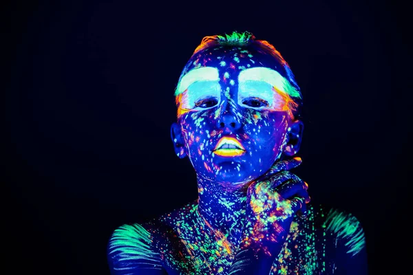 Portrait of beautiful girl with ultraviolet paint on her face. Girl with neon make-up in color light.