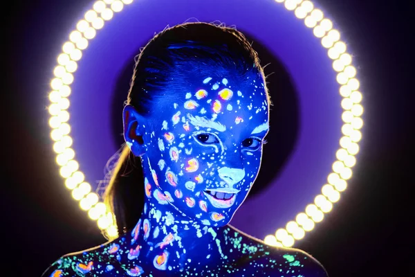 Retrato de una hermosa chica con pintura ultravioleta en su cara. Chica con maquillaje de neón en luz de color . —  Fotos de Stock