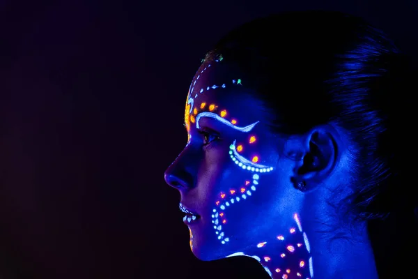 Retrato de una hermosa chica con pintura ultravioleta en su cara. Chica con maquillaje de neón en luz de color . —  Fotos de Stock