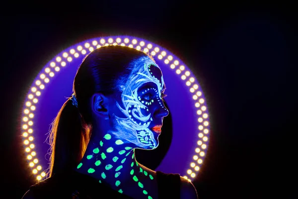 Retrato de una hermosa chica con pintura ultravioleta en su cara. Chica con maquillaje de neón en luz de color . —  Fotos de Stock