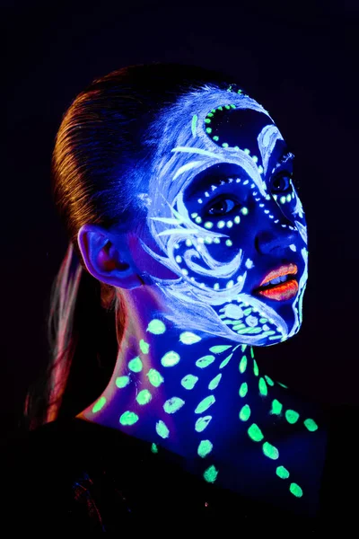 Portrait of beautiful girl with ultraviolet paint on her face. Girl with neon make-up in color light.