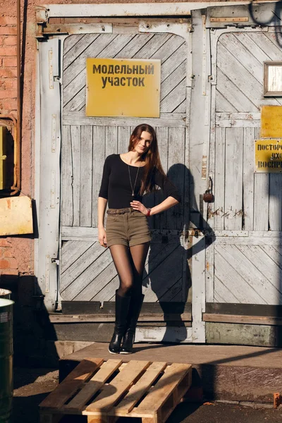Attraente ragazza in posa davanti alla porta della fabbrica con piastra di avvertimento . — Foto Stock