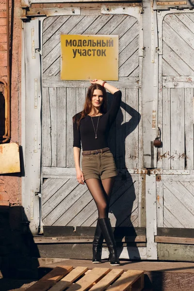 Attraktives Mädchen posiert vor Fabriktür mit Warnschild. — Stockfoto