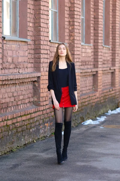 Street fashion, urban style. Girl in jacket, t-shirt, short skirt and high boots