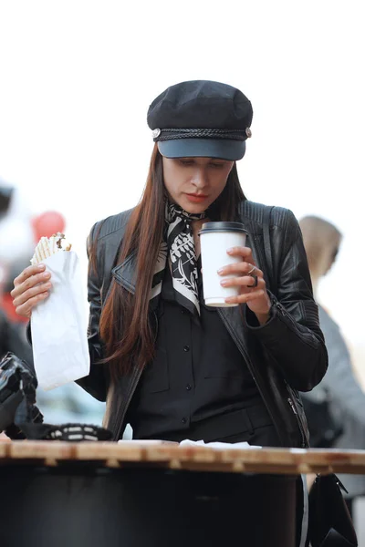Chica atractiva comer sándwich en la cafetería de la calle y leer noticias en el teléfono inteligente — Foto de Stock