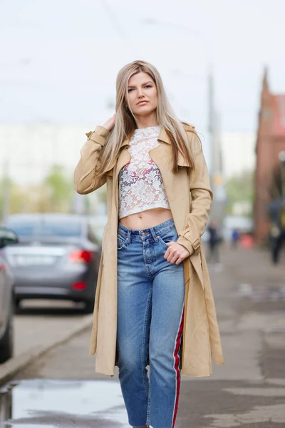 Jolie fille en jeans courts et imperméable marchant dans la rue après la pluie — Photo