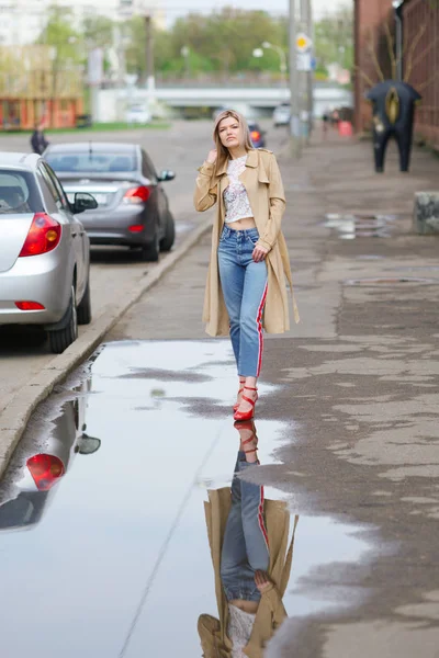 Jolie fille en jeans courts et imperméable marchant dans la rue après la pluie — Photo