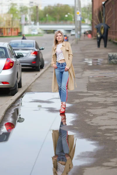 Hübsches Mädchen in kurzen Jeans und Regenmantel, das nach dem Regen auf die Straße läuft — Stockfoto