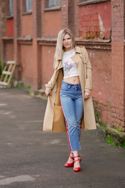 Bella ragazza in jeans corti e impermeabile che cammina per strada dopo la pioggia — Foto Stock