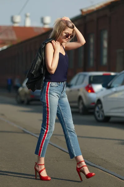 Nettes blondes Mädchen mit Sonnenbrille überquert die Straße mit Lederjacke in der Hand — Stockfoto