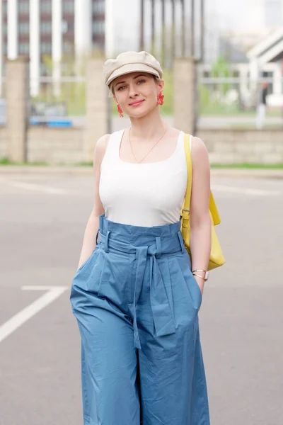 Девушка в квадратной шляпе, белый t shrt и синие широкие брюки ходьба на парковке автомобиля — стоковое фото
