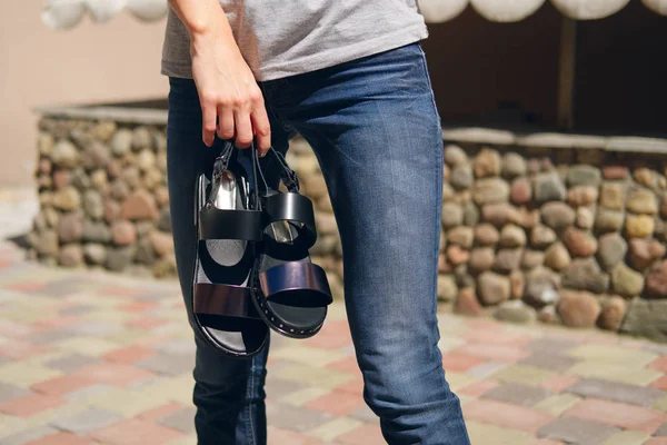 Menina irreconhecível em jeans segurando um par de sandálias na mão — Fotografia de Stock