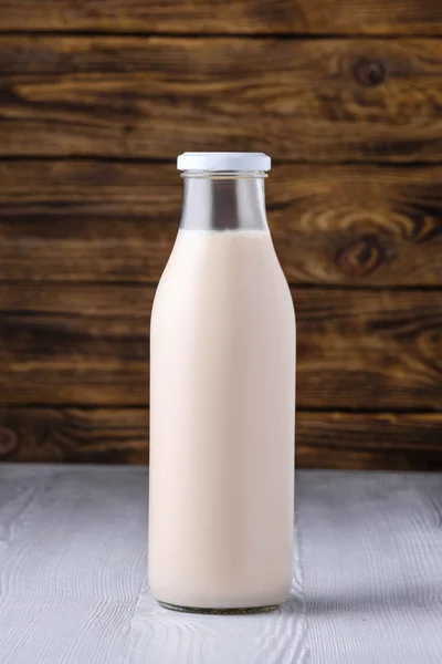Bottiglia di latte di soia su tavolo bianco su sfondo di legno scuro — Foto Stock