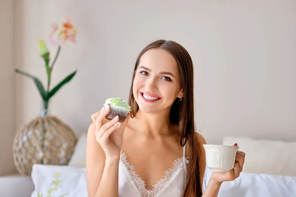 Cute girl eating cake and drinking tea in bed