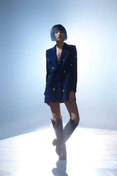 Fashion model with bob haircut in blue jacket with gems decor and in wide high boots on the stage under key light — 图库照片