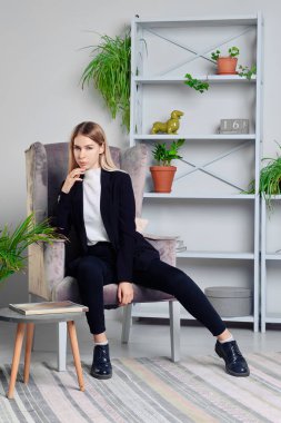 Kotlu ve ceketli kız çatı katında koltukta oturuyor.