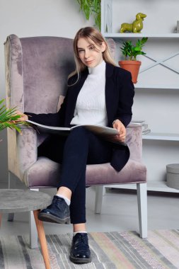 Dergi ile oturma odasında oturan kot pantolon ve ceket kız 