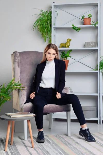 Chica en jeans y chaqueta sentada en sillón en loft — Foto de Stock