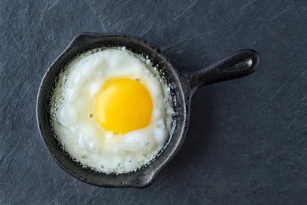 Вид сверху на жареное яйцо в маленькой чугунной сковороде. Делать яичницу . — стоковое фото