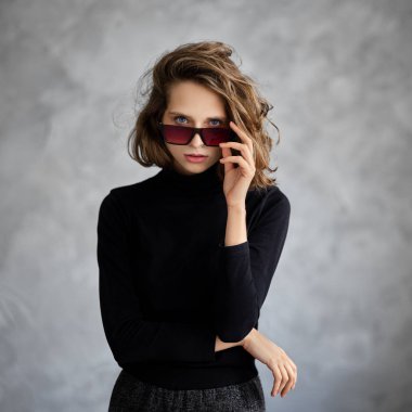 Curly-haired girl looks straight putting down sunglasses