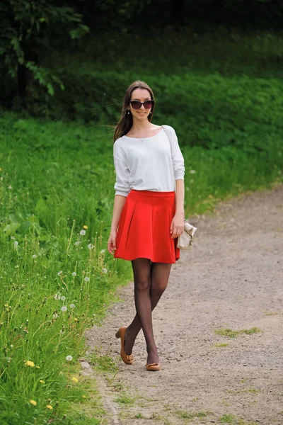 Портрет девушки в красной юбке и белой блузке, стоящей на тропинке в парке — стоковое фото