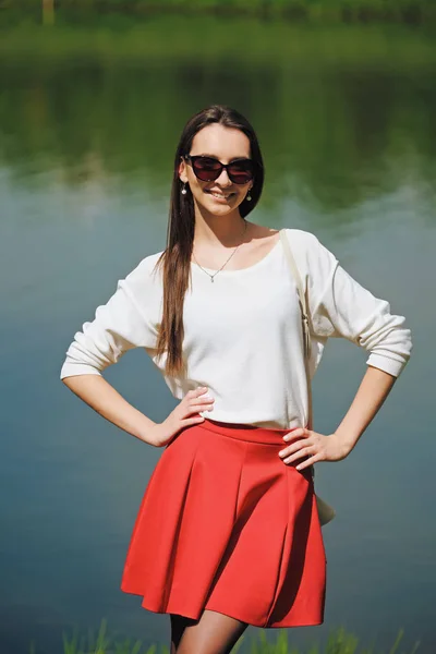 Retrato de una niña en falda roja y blusa blanca de pie en la orilla del río — Foto de Stock