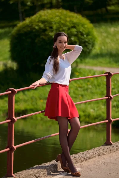 Ritratto di ragazza in gonna rossa e camicetta bianca appoggiata ad una ringhiera di ponte sulla riva del fiume — Foto Stock