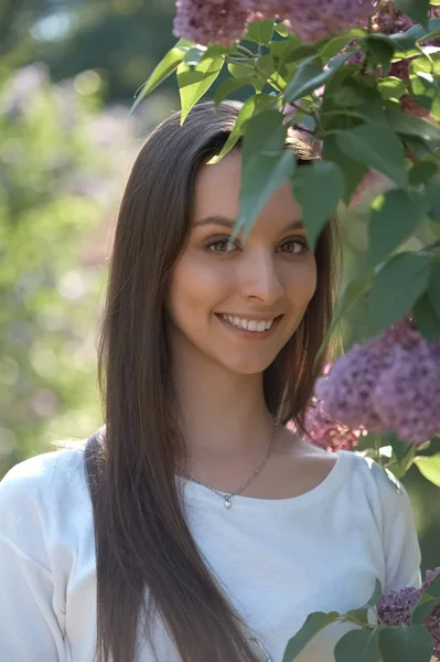 Retrato al aire libre de hermosa chica sonriente de pie entre arbustos lila — Foto de Stock