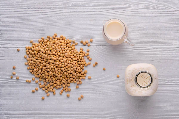 Vista superior de botella y jarra de leche de soja en mesa de madera blanca — Foto de Stock