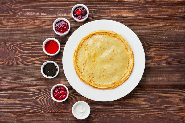 Bovenaanzicht van dunne pannenkoeken met assortiment jam en saus — Stockfoto