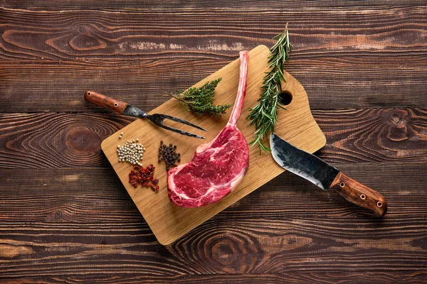 Bovenaanzicht van rauwe cowboy steak op houten snijplank met kruid — Stockfoto