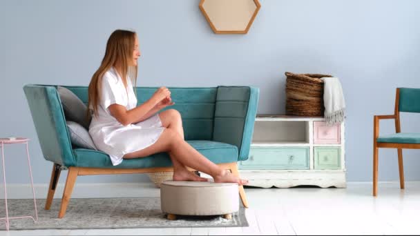 Menina Bonita Aplicando Creme Casa Sentado Sofá Robe Seda Branca — Vídeo de Stock