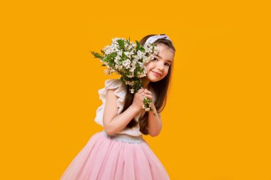 Parlak sarı arka planda elinde bahar çiçekleri olan neşeli bir çocuk.