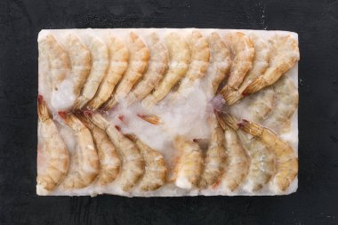 Siyah zemin üzerinde büyük bir buz küpünün içinde donmuş çiğ kaplan karidesi.