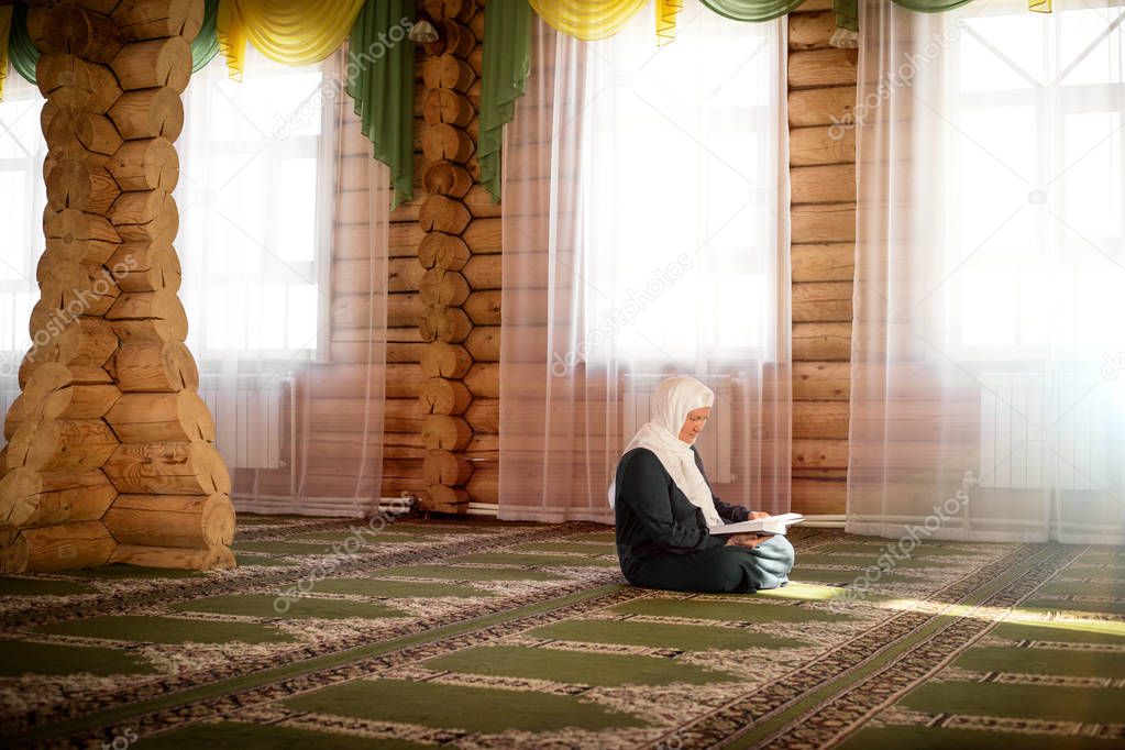 Elderly woman praying in the mosque and reading the Quran