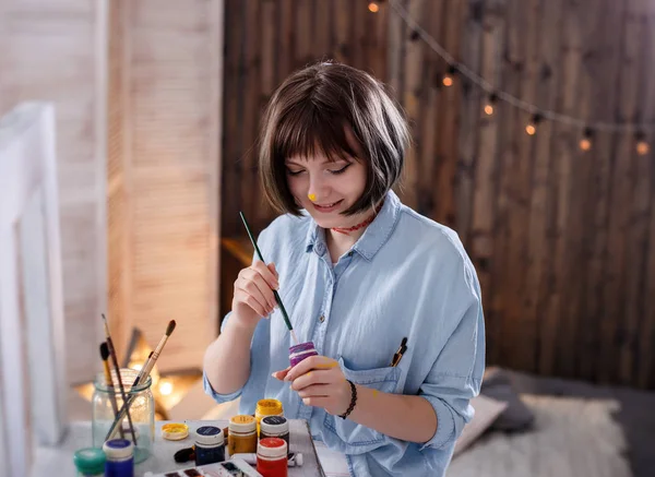 Joven pintora sosteniendo pincel, sonriendo y pintando un cuadro — Foto de Stock