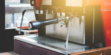 Profesyonel bir barista kahve makinesini müşterinin siparişiyle kahve yapmak için kullanır. Kahve dükkanı eski moda, güneş ışığıyla süslenir.