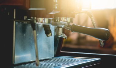 Profesyonel bir barista kahve makinesini müşterinin siparişiyle kahve yapmak için kullanır. Kahve dükkanı eski moda, güneş ışığıyla süslenir.
