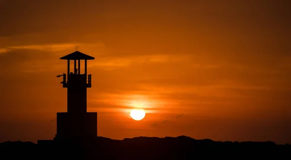 silhouette light house with the Sun falls on the sea at sunset time