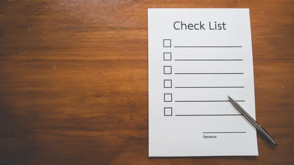 Flat lay and  Top view of Check list paper with pen on wooden table in business concept,vintage style