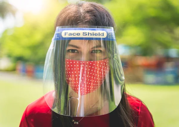 Women wearing Face shield, Asian women use face protection and cloth masks to prevent infection and reduce risk during the outbreak and use a New Normal lifestyle with blur public park background