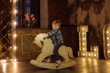 Red-haired boy on a rocking horse.Photoshoot in the studio.Fairytale Photography clipart