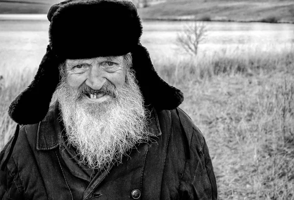 Toothless old man with a beard in a winter hat. Black and white photography